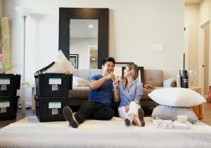 Dicas para tornar seu imóvel mais atrativo para locação: casal feliz se preparando para morar, com caixas de mudança em uma sala moderna e aconchegante.