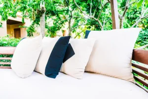 Imagem de móveis de jardim com almofadas na varanda, com vegetação ao fundo, destacando cuidados para prolongar a vida útil dos móveis de jardim.