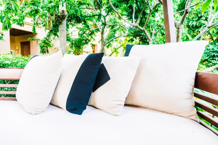 Imagem de móveis de jardim com almofadas na varanda, com vegetação ao fundo, destacando cuidados para prolongar a vida útil dos móveis de jardim.