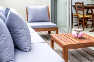 Móveis de área externa com materiais duráveis, incluindo sofá de madeira com almofadas cinza, mesa de centro de madeira e cadeiras na varanda.