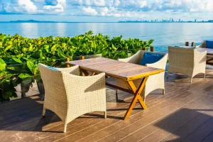 Imagem de móveis multifuncionais para otimizar áreas externas em uma varanda com vista para o mar, com mesa de madeira e cadeiras de fibra sintética tropical, ideal para relaxar e aproveitar momentos ao ar livre.