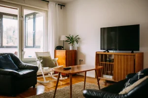Imagem de sala de estar com sofá preto, TV na parede, cadeira de balanço e decoração moderna, ideal para entender o que considerar ao alugar um imóvel comercial.
