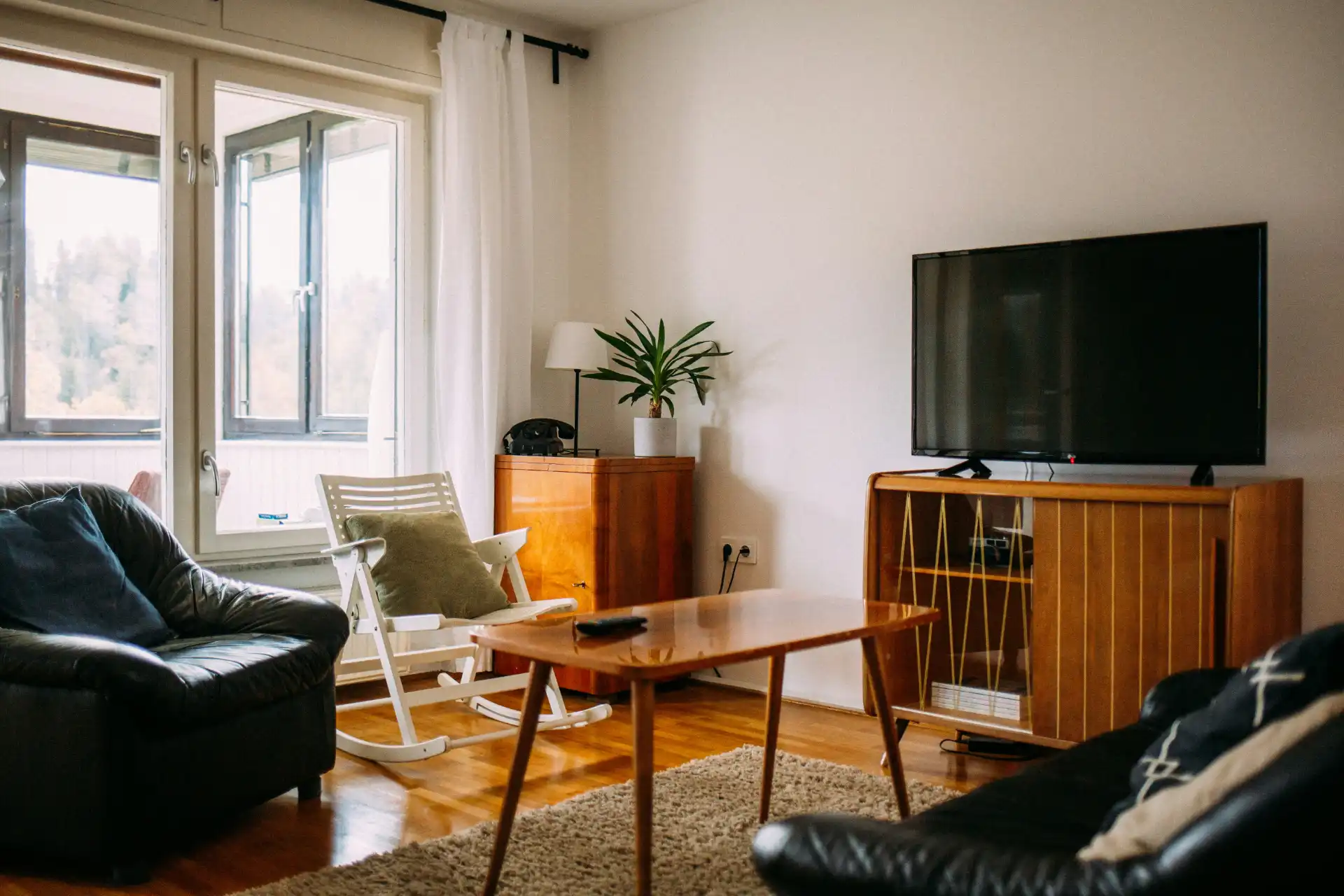 Imagem de sala de estar com sofá preto, TV na parede, cadeira de balanço e decoração moderna, ideal para entender o que considerar ao alugar um imóvel comercial.
