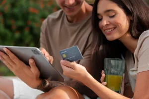 Casal sorridente usando cartão de crédito e celular para aprender dicas para aumentar o limite do cartão de crédito