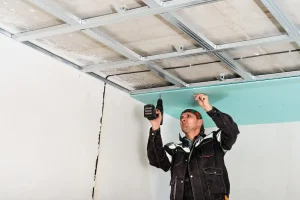 Instalador de forro de PVC, drywall e gesso em andamento com ferramentas elétricas em obra residencial, comparando diferenças de materiais.