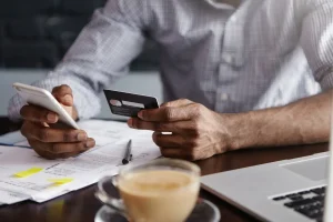 Pessoa verificando fatura de cartão de crédito com documento e smartphone, preocupado com erro na cobrança.